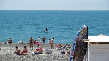 İnsanlar SOCHI plajında güneşleniyor ve dinleniyor - Haziran 2021. Karadeniz 'de yaz mevsiminin başlangıcı. Sahildeki deniz dalgalarında SUP üzerinde yüzen insanların silueti.. 