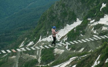 Rusya 'nın Soçi kentinde, Rosa Tepesi' nde (2320 metre) halat asma köprüsü üzerinde yürüyen turistler görülüyor. Uçurumun üzerinde asılı duran insanlar, aşırı cazibe. Güzel manzara, dağların zirvesi bulutlar ve karlar içinde.