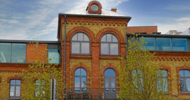 Kemerli pencereleri ve modern cam uzantılarıyla yenilenmiş tarihi tuğla bina. Klasik ve çağdaş şehir mimarisinin bir karışımı..