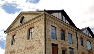 Tarihi taş bina cephesi, yenilenmiş. Geleneksel kemerli pencereler, hafif tuğlalar, modern siyah yatakhaneler ve gösterişli çatı. Şehir mimarisi karışımı. Emlak, kentsel yaşam ve emlak pazarlama.