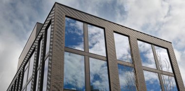 Modern bina dışı, geniş yansıtıcı pencereler mavi gökyüzünü ve bulutları gösteriyor. Minimalist şehir tarzı gayrimenkul, konut dairesi, ofis mimarisi