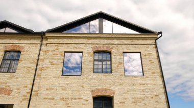 Tarihi taş bina cephesi, yenilenmiş. Geleneksel kemerli pencereler, hafif tuğlalar, modern siyah yatakhaneler ve gösterişli çatı. Şehir mimarisi karışımı. Emlak, kentsel yaşam ve emlak pazarlama