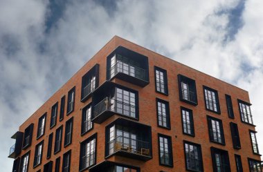 Sıcak tuğla kaplamalı ve siyah çerçeveli Fransız pencereli çağdaş apartman cephesinde tekrar eden balkonlar yer alıyor. Emlak, kentsel yaşam ve emlak pazarlama.