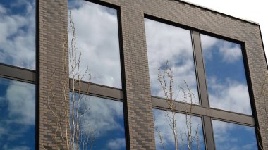 Geniş yansıtıcı pencereli modern tuğla cephesi mavi gökyüzünü ve bulutları gösteriyor. Temiz fotokopi alanı olan alçak açı. Minimalist şehir tarzı gayrimenkul, konut dairesi, ofis mimarisi