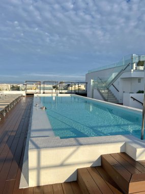 Ahşap döşemeli, güneşli ve şehir manzaralı lüks dikdörtgen çatı havuzu. Modern şehir oteli ve yaz tatili konsepti.