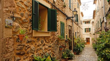 Valldemossa 'da kır taşı evleri ve yeşil kepenkleri olan dar bir kaldırım taşı caddesi. Geleneksel Mallorcan köy sokağı saksı bitkileriyle süslenmiş..