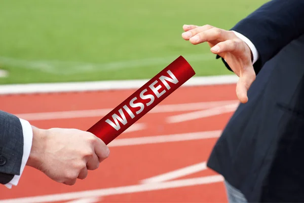 Businessmen passing baton in relay race with German word Wissen means Knowledge — Stock Photo, Image