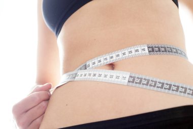 Genç zayıf kadın spor yaptıktan sonra kalça çevresini ölçüyor.