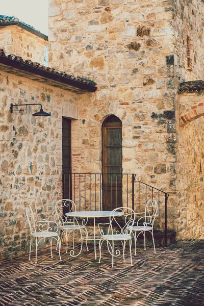 Small table with white chairs outside a brick and stone house in an old Italian village. Vintage scene.