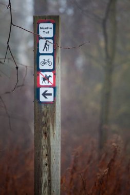 Indications path in the forest. Orientation pole. Meadow trail. Wooden pole above signals and signs to the trail in the meadow in the forest. Fog in the winter season. Location: Ontario, Canada.