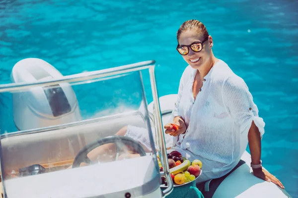 Smiling woman on boat in the sea with fruit. The young woman is wearing sunglasses. Blue sea.