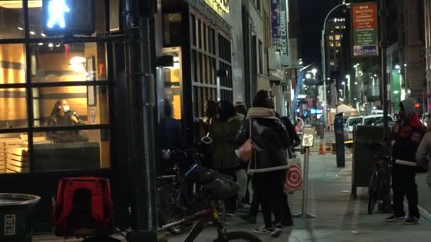 НЬЮ-ЙОРК, США - 23 ЯНВАРЯ 2021 года: Люди в масках ждут в очереди, чтобы войти в кафе ночью. Средний Манхэттен — стоковое видео