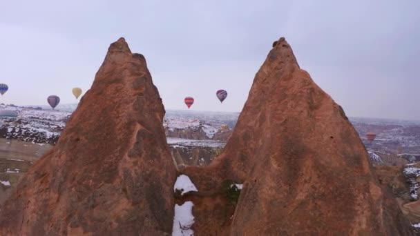 CAPPADOCIA, TURKEY - 2021年4月10日：冬季早晨在雪地卡帕多西亚的热气球。土耳其。空中景观。无人机在柱子间飞驰而过 — 图库视频影像