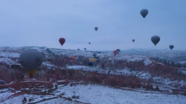 CAPPADOCIA, TURKEY - 10. dubna 2021: Horkovzdušné balóny v zasněžené Cappadocii v zimním ránu. Krocan. Letecký pohled. Dron letí nahoru — Stock video