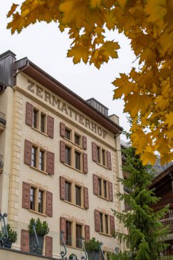 ZERMATT, SWitzERLAND - 20 Ekim 2025: Bulutlu bir günde Grand Hotel Zermatterhof ve Sarı Akçaağaç Dalları. Zermatt, Valais, İsviçre