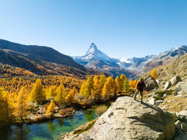 Kayanın tepesindeki yürüyüşçü Matterhorn Dağı 'na bakıyor. Sunny Day 'de Grindjisee Gölü ve Yellow Larches. Sonbahar Renkleri. İsviçre Alpleri. Hava görüntüsü. Zermatt, Valais, İsviçre