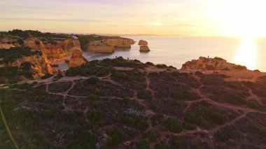 Güneşli bir günde Marinha Sahili, Kayalıklar, Deniz Yığınları ve Atlantik Okyanusu. Yeşil çalılık. Hava görüntüsü. Algarve, Portekiz. İleriye ve yukarıya doğru ilerliyoruz. Görüntü Görüntüsü
