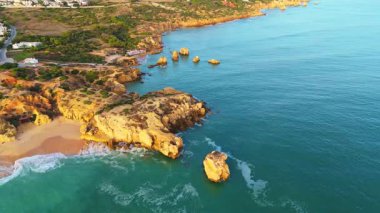 Burunlar, uçurumlar, deniz yığınları ve Arrifes plajı. Güneşli bir günde kıyı şeridi ve Atlantik Okyanusu. Yeşil Ağaçlar. Havadan çekim. Algarve, Portekiz. İnsansız Hava Aracı İleri, Eğiliyor