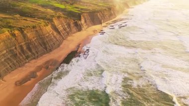 Low Tide sırasında Sunset 'te Magoito Sahili ve Dik Kayalıklar. Dramatik Gökyüzü ve yemyeşil çayırlar. Atlantik Okyanusu, Portekiz. Altın Saat. Hava görüntüsü. İlerleyin, ilerleyin. Görüntü Görüntüsü