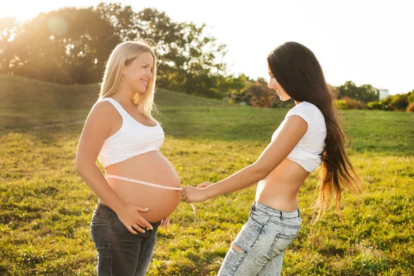 Jovem mulher medindo a barriga de sua amiga grávida . — Fotografia de Stock