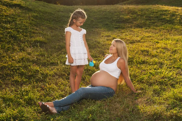 Cute little girl watering her mother's belly. — Stock Photo, Image