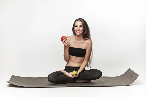 Mujer joven muy atractiva sentada en una esterilla de yoga — Foto de Stock