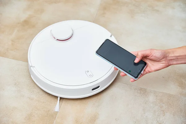 Akıllı telefonu uygulama kontrol robotu elektrikli süpürgesiyle tutuyor.