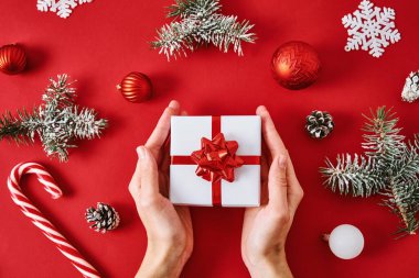 Bir kadının ellerinde şenlik kurdelesi ve kırmızı arka planda Noel süslemeleri.