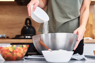 Mutfakta hamur pişiren bir kadın. Eller bir kaseye un döker.