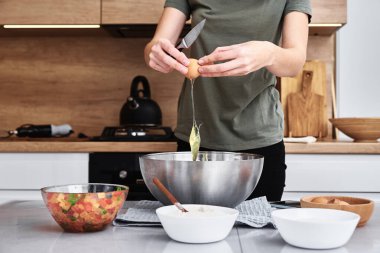 Mutfakta hamur pişiren bir kadın. Eller yumurtayı kaseye kırar.