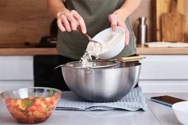 Mutfakta hamur pişiren bir kadın. Eller bir kaseye un döker.