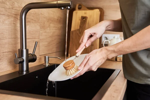 Woman washes dishes with wooden eco friendly brush. Zero waste concept
