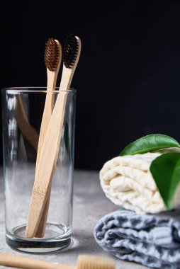 Bambu diş fırçaları, cam ve banyo havluları, koyu bir arka plan.