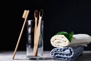 Bambu diş fırçaları, cam ve banyo havluları, koyu bir arka plan.