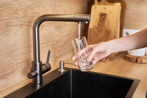 Woman pouring clean water from tap filter into a glass