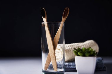 Bambu diş fırçaları, cam ve banyo havluları, koyu bir arka plan.