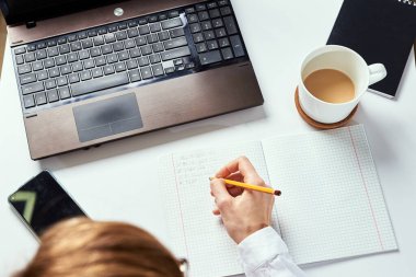 Uzaktan kumanda. Kadın not defterine not alır ve çalışmak için dizüstü bilgisayar kullanır. Uzaklık eğitimi ve e-öğrenme kavramı