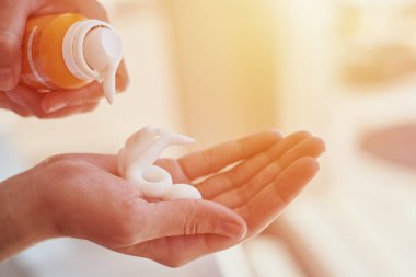 Kadın elleri güneş kremi şişesinden güneş kremi sürüyor.