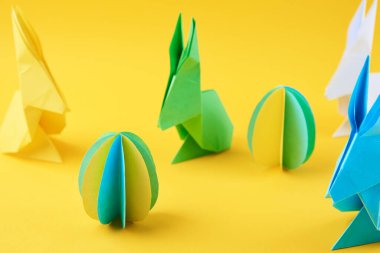 Kağıt origami Esater tavşanları ve sarı arka planda renkli yumurtalar, üst manzara. Paskalya kutlaması kavramı