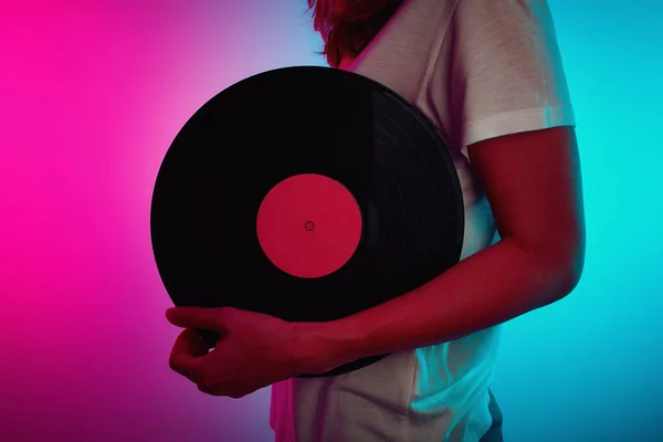 Woman holds retro vinyl disc with neon light