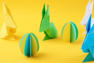 Kağıt origami Esater tavşanları ve sarı arka planda renkli yumurtalar, üst manzara. Paskalya kutlaması kavramı