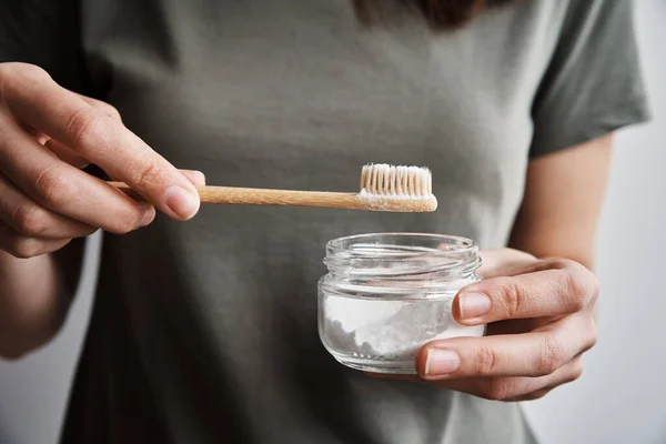 Mujer sostiene cepillo de dientes de bambú y polvo de soda en sus manos — Foto de Stock