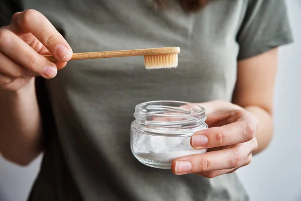 Mujer sostiene cepillo de dientes de bambú y polvo de soda en sus manos — Foto de Stock