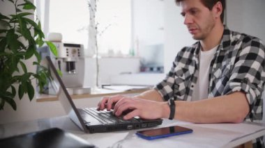 Adam ev ofisinde dizüstü bilgisayar ve belgelerle çalışıyor.