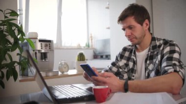 Adam ev ofisinde dizüstü bilgisayar ve belgelerle çalışıyor.