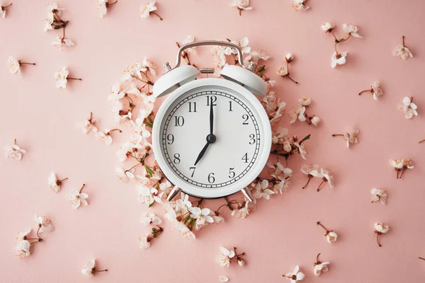 Relógio despertador sobre fundo rosa com flores. Conceito de tempo de mudança — Fotografia de Stock