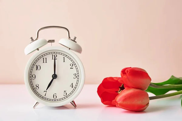 Relógio despertador e flores em vaso sobre fundo branco — Fotografia de Stock
