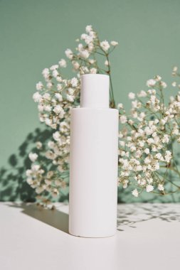 Yeşil arka planda bitkili doğal kozmetik krem şişesi.