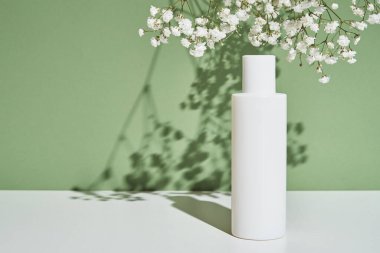Yeşil arka planda bitkili doğal kozmetik krem şişesi.