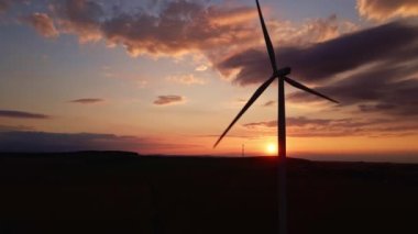 Gün batımında tarlada yel değirmeni türbini silueti. Dönen rüzgar jeneratörü